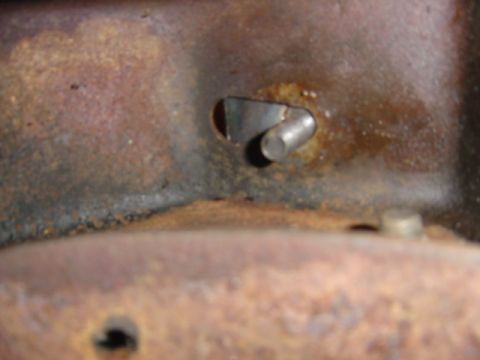 1986 Ford Bronco - Close-up of a corroded metal bracket with a pin, showing signs of wear and tear.