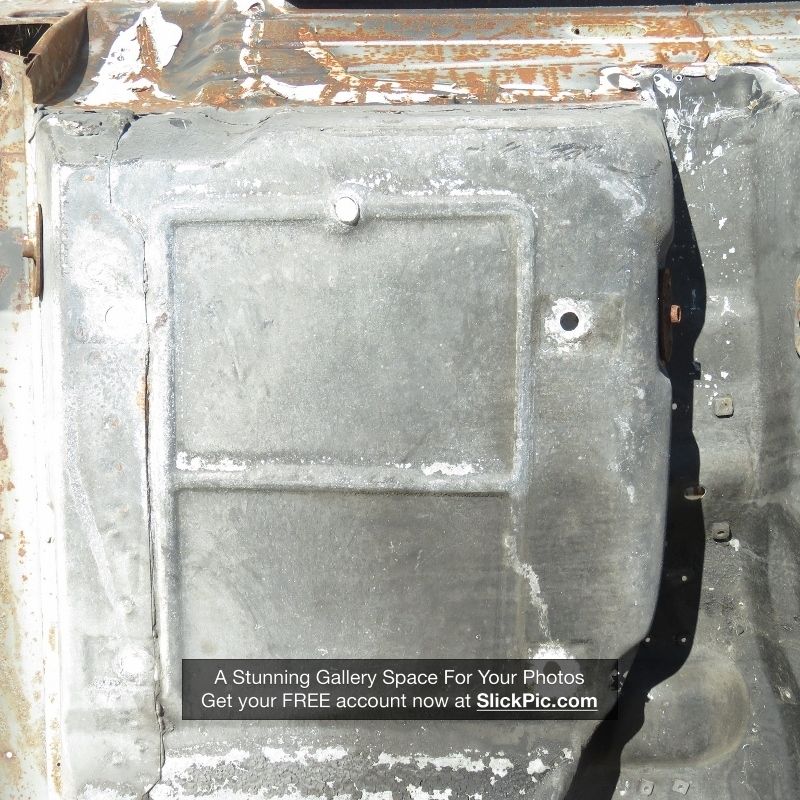 Undercarriage of a damaged vehicle, showing a metal panel with a raised rectangular section and a circular hole