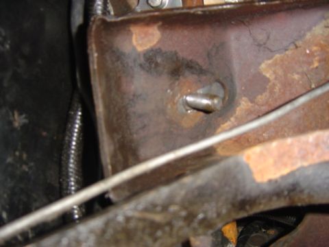 1986 Ford Bronco - Close-up view of a rusted metal bracket with a bolt and a cable, likely from a vehicle's undercarriage.
