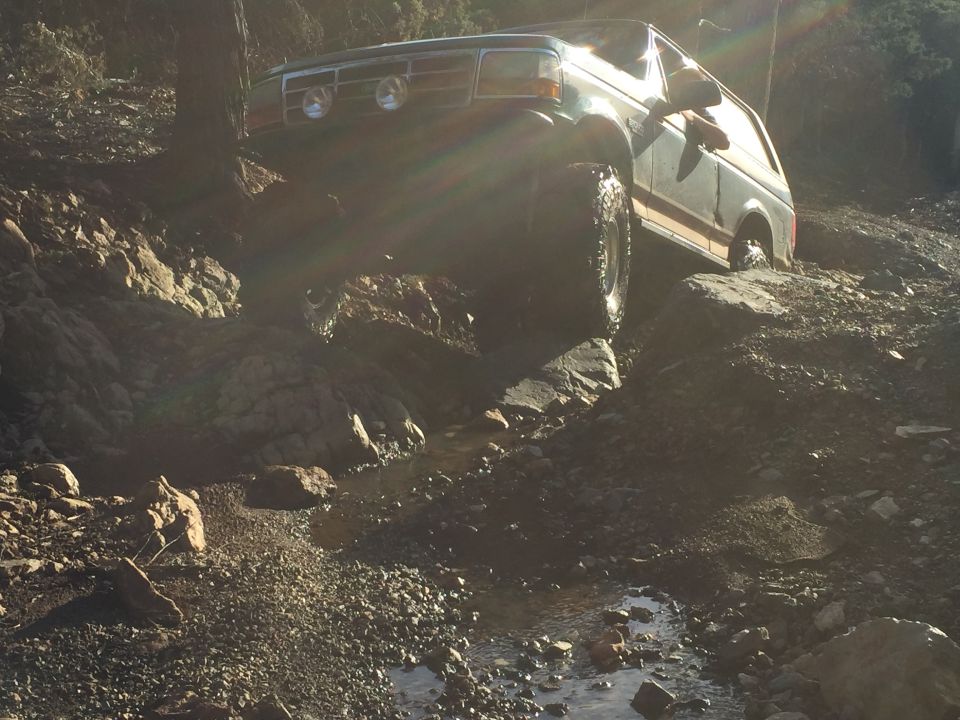 1994 Ford Bronco off-roading on a rocky trail with a stream.