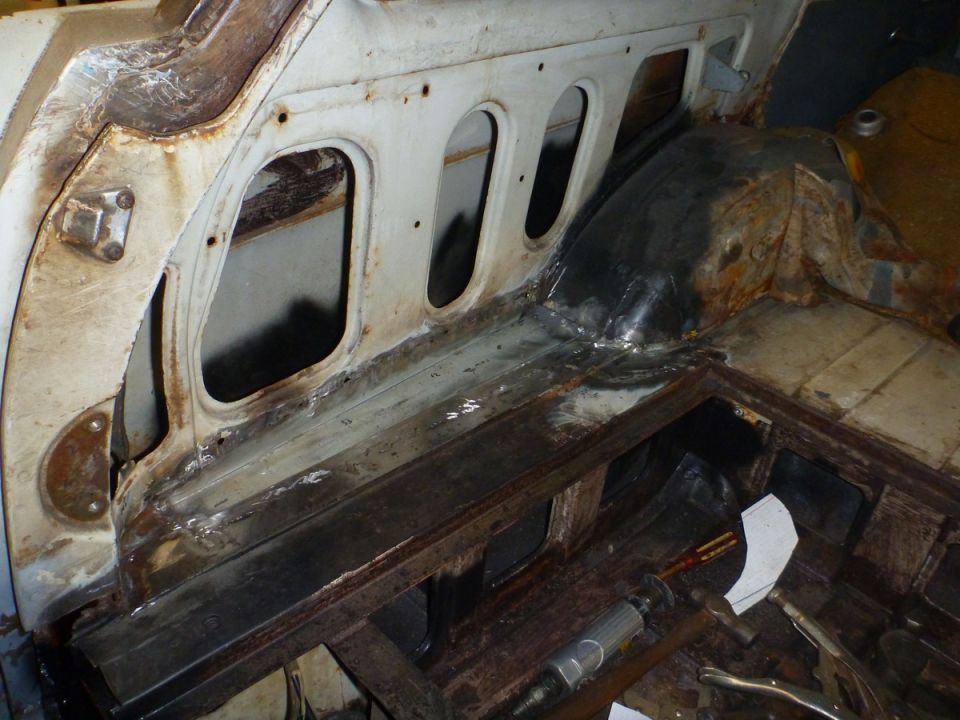 Interior rear of a classic car with rust and welding repairs on floor and wheel well.