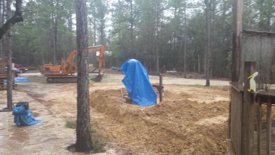 Orange excavator in a muddy construction site with trees and a blue tarp.