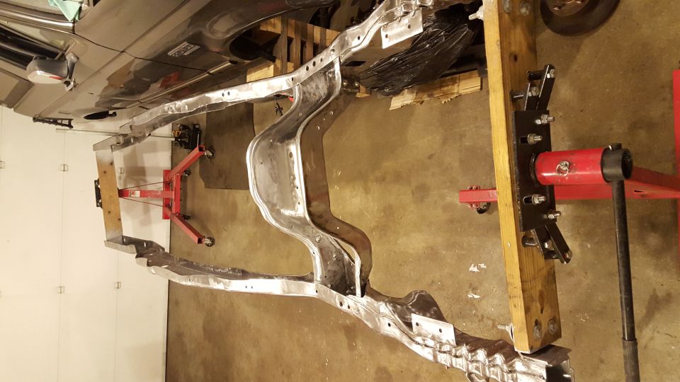 Bare metal vehicle frame suspended by shop equipment, possibly a 1994 Ford Bronco frame.