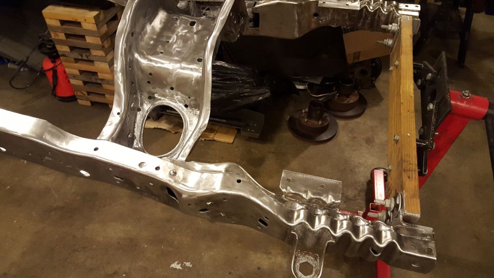 Bare metal vehicle frame, possibly 1994 Ford Bronco, in a workshop.