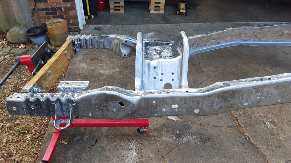 Bare metal truck frame on red jack stands and wooden brace, ready for restoration.