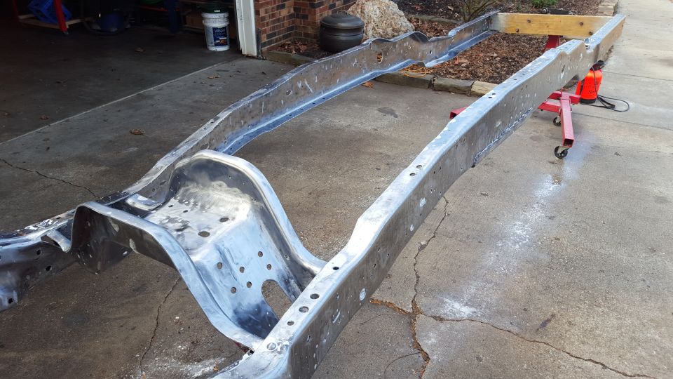 Bare metal truck frame on a red engine stand, outdoors.