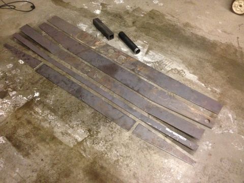 1979 Ford Bronco - Several pieces of cut metal are laid out on a concrete floor. Two short pieces of square tubing and one cylindrical piece are also visible.