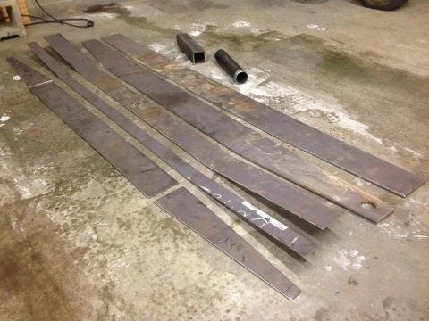 1979 Ford Bronco - Several pieces of cut metal, including long flat bars and two short hollow metal tubes, are laid out on a concrete floor.