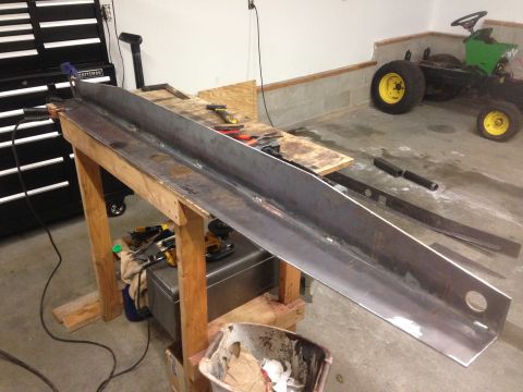 1979 Ford Bronco - A long, heavy-duty metal beam with holes drilled in it is resting on a wooden workbench. Tools and a small green tractor are visible in the…