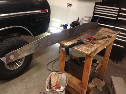 1979 Ford Bronco - A long, flat piece of metal is positioned over the rear tire and wheel well of a black vehicle, resting on a wooden workbench. Tools such a…