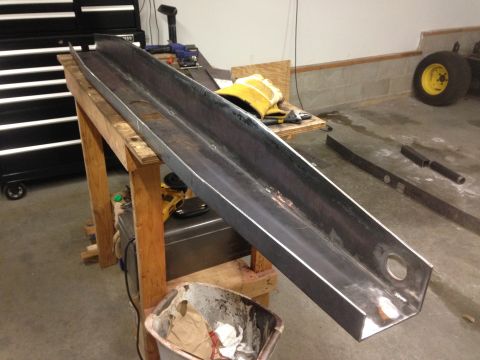1979 Ford Bronco - A long, C-shaped metal beam is resting on a wooden workbench. Various tools and a yellow glove are visible on a smaller wooden surface behi…