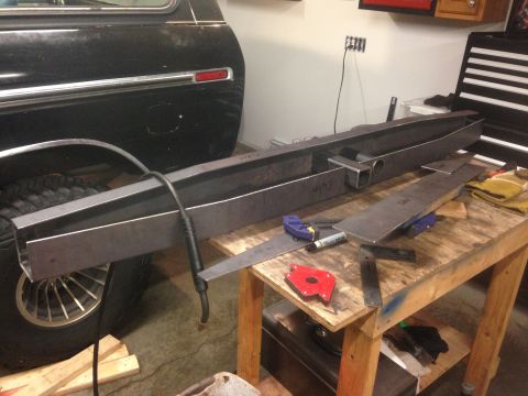 1979 Ford Bronco - A black vehicle, possibly an SUV, is partially visible on the left. In the foreground, custom metal fabrication parts are laid out on a wor…