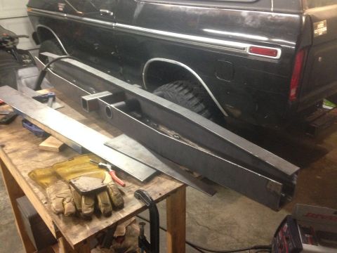 1979 Ford Bronco - A custom fabricated metal bumper is laid out on a workbench in front of the rear quarter panel of a black 1970s era Ford Bronco. Welding gl…