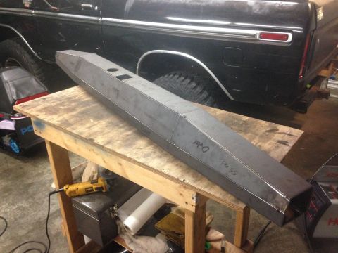 1979 Ford Bronco - A custom-fabricated steel bumper is shown resting on a workbench in front of a black Ford Bronco. The bumper is long and angular, with cuto…