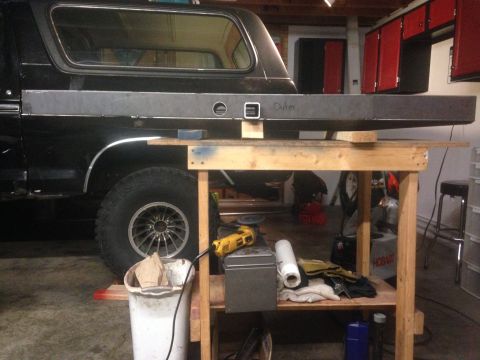 1979 Ford Bronco - A black Ford Bronco is parked in a garage next to a workbench where a metal panel is being worked on. The metal panel has the word "Outer"…
