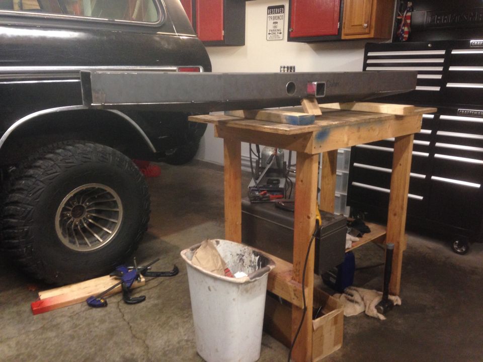 Custom steel bumper on workbench next to black SUV rear tire and fender.