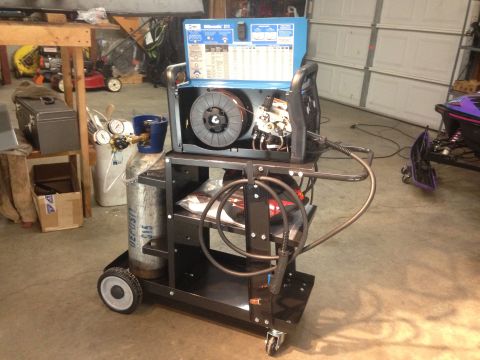 1979 Ford Bronco - A welding cart with a MillerMatic 211 welder, a gas cylinder, and welding accessories is parked on a concrete floor in a garage. A snowmobi…