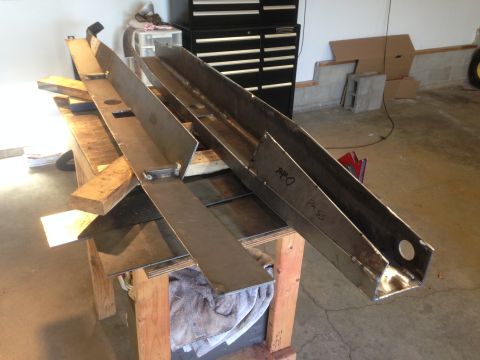 1979 Ford Bronco - Two long, fabricated steel frame rails are laid out on a workbench, possibly for a custom vehicle build. One rail has handwritten text that…