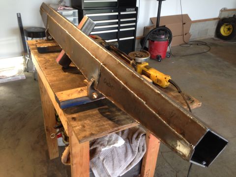 1979 Ford Bronco - A long, welded steel beam is resting on a wooden workbench. An angle grinder is positioned on the beam, and a red shop vac is visible in th…
