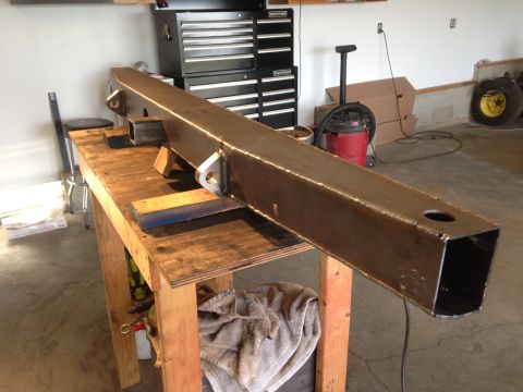 1979 Ford Bronco - A custom-fabricated steel bumper or frame component is shown resting on a wooden workbench in a garage setting. The heavy metal piece has s…