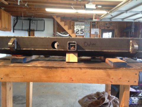 1979 Ford Bronco - A heavy-duty metal bumper, possibly for a truck or SUV, is shown resting on a wooden workbench in a garage. The bumper has two circular cut…