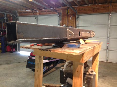 1979 Ford Bronco - A large, fabricated steel bumper or frame component is shown resting on a wooden workbench in a garage. A snowmobile is partially visible b…