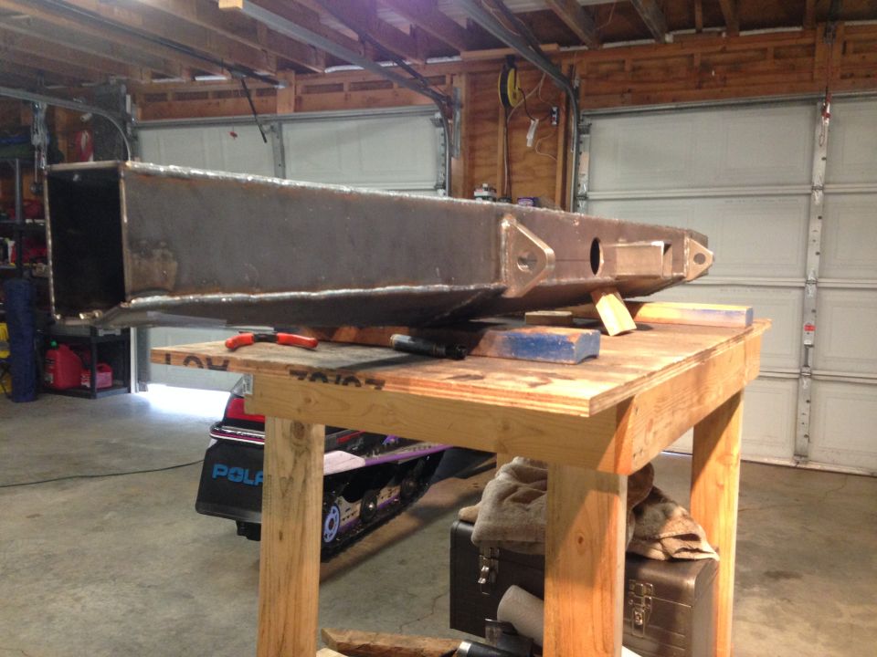 Fabricated steel bumper on workbench with snowmobile below in garage.