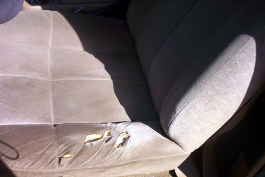 Worn tan cloth bench seat with torn fabric and exposed foam