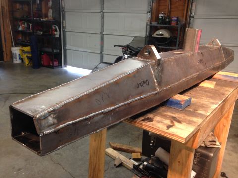 1979 Ford Bronco - A fabricated steel component, possibly a bumper or frame extension, rests on a wooden workbench in a garage. The component has visible weld…