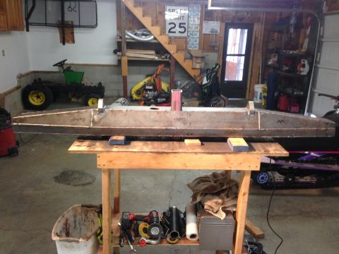 1979 Ford Bronco - A long, fabricated metal part, possibly a frame or bumper, is supported by a wooden table in a garage setting. Tools and other equipment ar…
