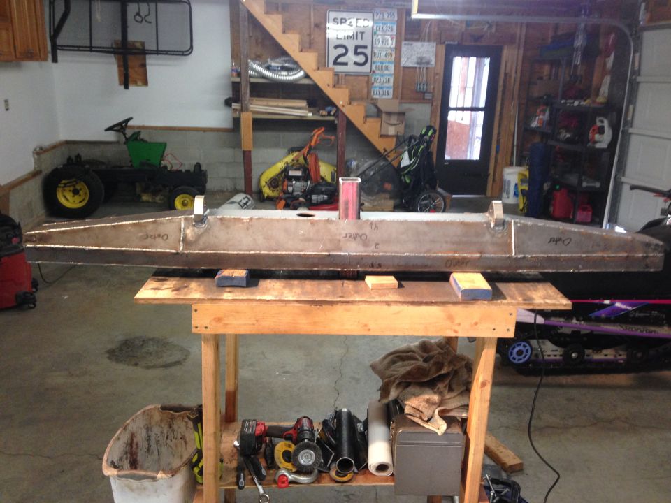Fabricated metal part on a workbench in a garage with a tractor and shelves in the background.