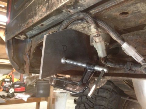 1979 Ford Bronco - A metal bracket, marked with the letter 'D', is clamped to the underside of a vehicle frame. Electrical connectors and wiring are visible a…