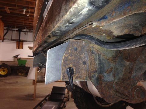 1979 Ford Bronco - A close-up, low-angle view of the heavily rusted frame and undercarriage of a vehicle, showing newly installed metal brackets on the frame…