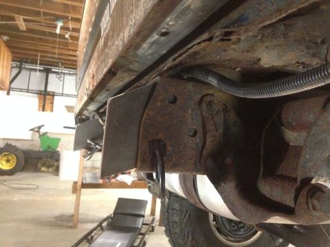 1979 Ford Bronco - Close-up view of the heavily rusted frame and suspension components of a vintage vehicle, possibly a Ford Bronco, in a workshop setting. Cu…