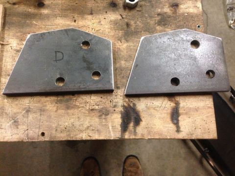 1979 Ford Bronco - Two metal brackets with three holes each are laid out on a wooden workbench. One bracket has the letter "D" written on it in black marker.
