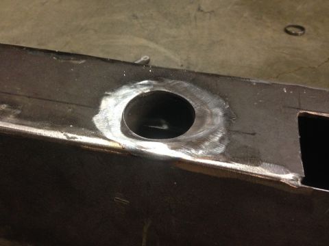 1979 Ford Bronco - A close-up view of a circular hole cut into a dark metal rectangular beam, likely a vehicle frame component. The edges of the hole show sig…