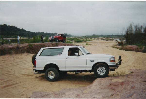 1995 Ford Bronco parked on sand with a red Jeep in the background