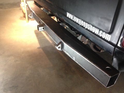 1979 Ford Bronco - A close-up, low-angle shot shows the rear of a vehicle with a custom-fabricated steel bumper. The bumper features a receiver hitch and two…