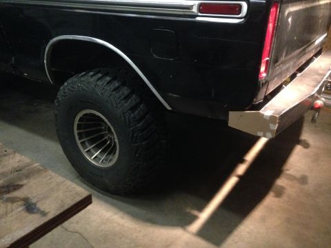 1979 Ford Bronco - The rear passenger side of a black pickup truck is shown, featuring a large off-road tire and a custom metal bumper that is currently under…