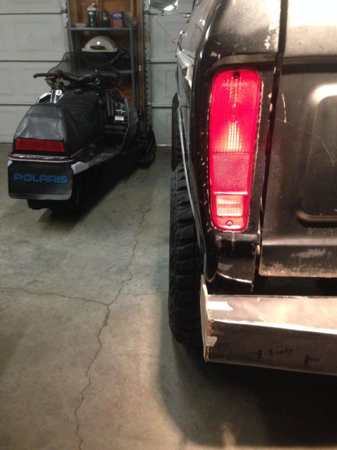 1979 Ford Bronco - The rear driver's side of a black Ford Bronco is shown parked next to a black Polaris snowmobile in a garage. The Bronco has a custom metal…