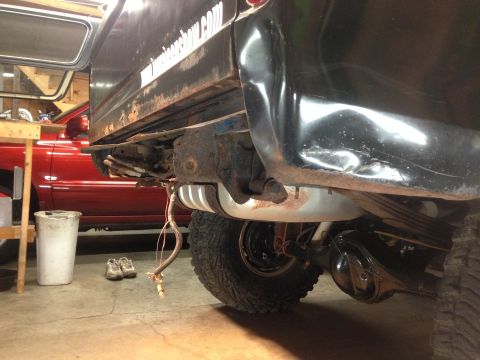 1979 Ford Bronco - The rear underside of a black vehicle, likely a truck or SUV, is shown with a rusty frame, a fuel tank, and suspension components. A red ve…