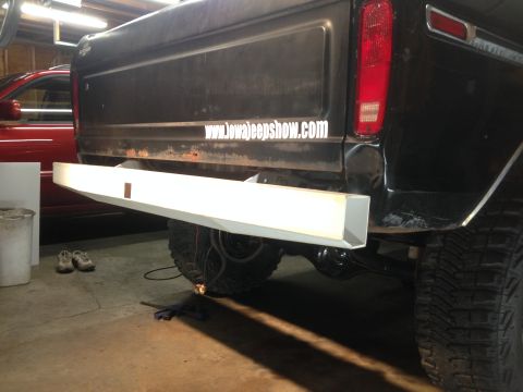 1979 Ford Bronco - The rear of a black Ford pickup truck is shown in a garage setting. A white aftermarket bumper is installed, and a sticker on the tailgate…