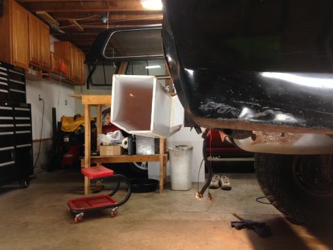 1979 Ford Bronco - A black vehicle's rear quarter panel is shown from a low angle in a garage setting. Wires hang down from the underside of the vehicle, and…