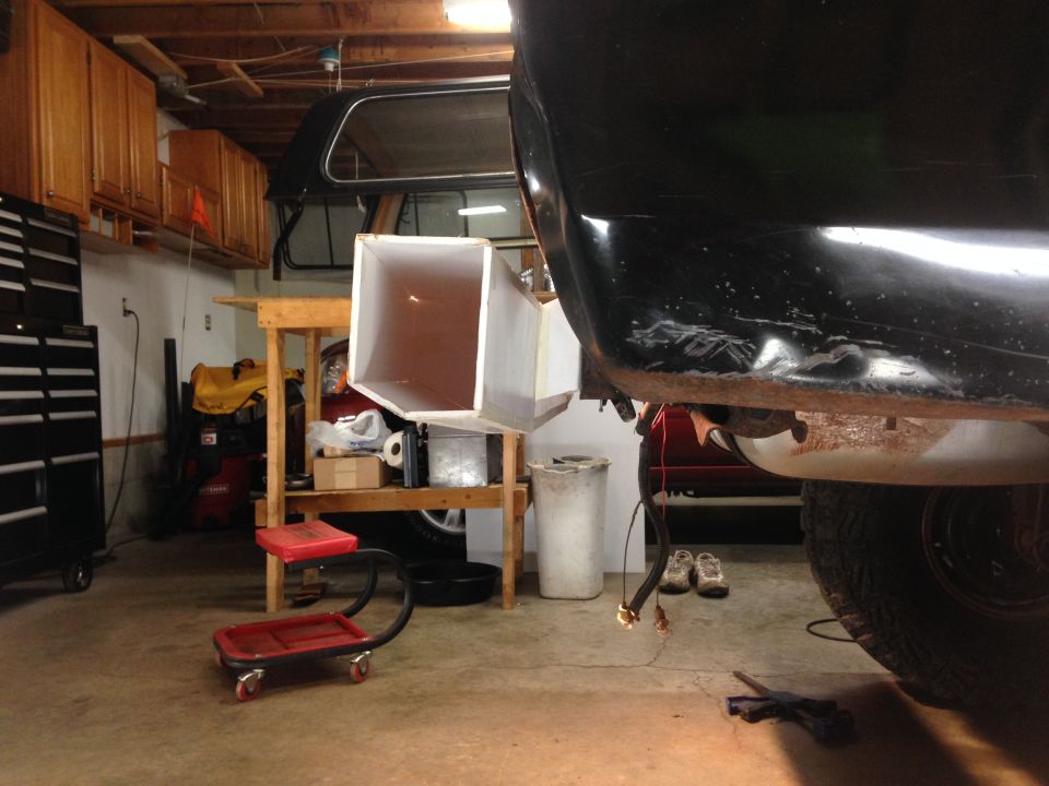 Black vehicle rear quarter panel with wires hanging down, white funnel attached to a stand in a garage.