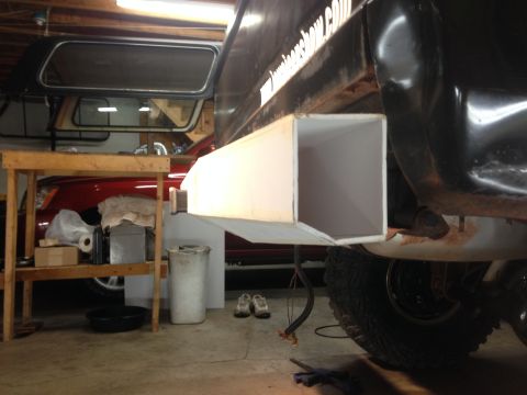 1979 Ford Bronco - The rear driver's side of a black Ford Bronco is shown in a garage setting. A custom white exhaust or storage box is attached to the rear b…