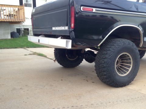 1979 Ford Bronco - The rear driver's side of a black Ford pickup truck is shown with a white aftermarket bumper and large off-road tires. The truck is parked…