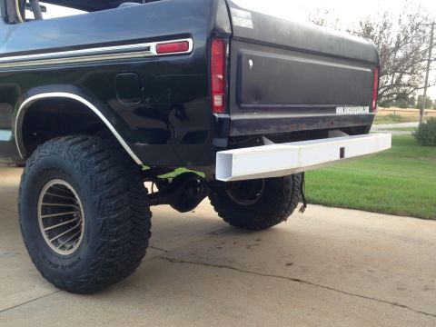 1979 Ford Bronco - The rear driver's side quarter view of a black Ford Bronco with a custom white metal rear bumper. It has large off-road tires and is parked…