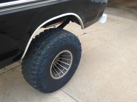 1979 Ford Bronco - Close-up of a large off-road tire and wheel on a black SUV.