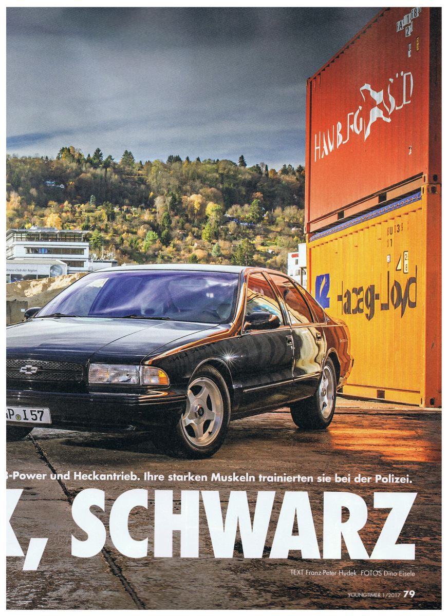 Black sedan with gold trim and a Chevrolet badge parked next to shipping containers