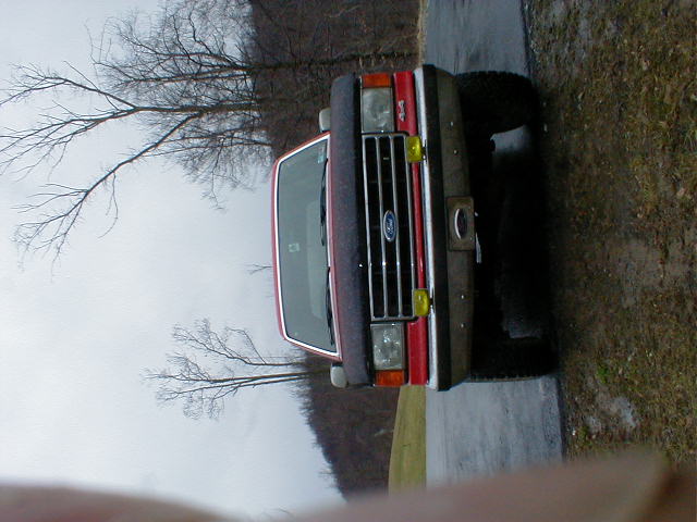 Red Ford Bronco parked outside, front view. Bare trees in background